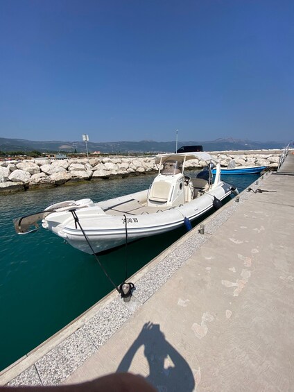 A white motorboat docked at a pier with a clear blue sky and distant mountains in the background. 3