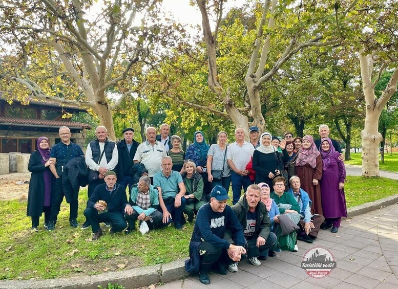 A group of people gathered outdoors, possibly for a community event, with trees and a building in the background. 5