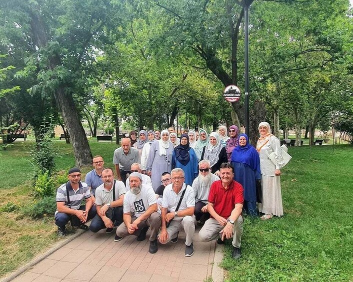 A group of people posing in a park with trees and a paved walkway. 2