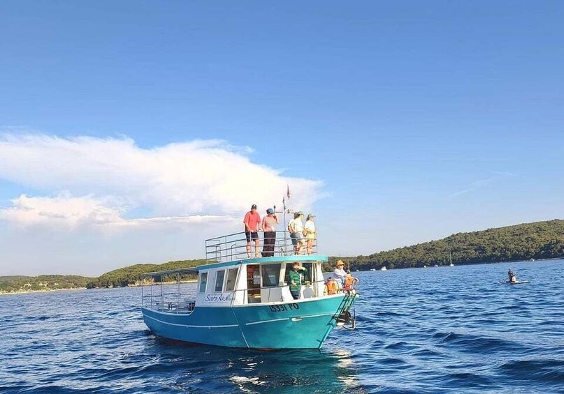 A blue boat with people on deck, surrounded by calm water and a hilly landscape in the background. 2
