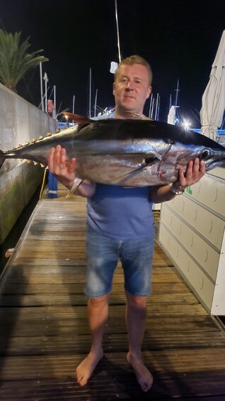 A person holding a large fish on a wooden dock at night. 1