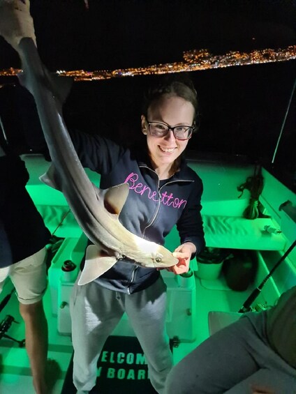 A person holding a fish on a boat with a cityscape in the background. 5