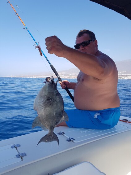 A person holding a fish on a boat with a clear sky and water in the background. 2