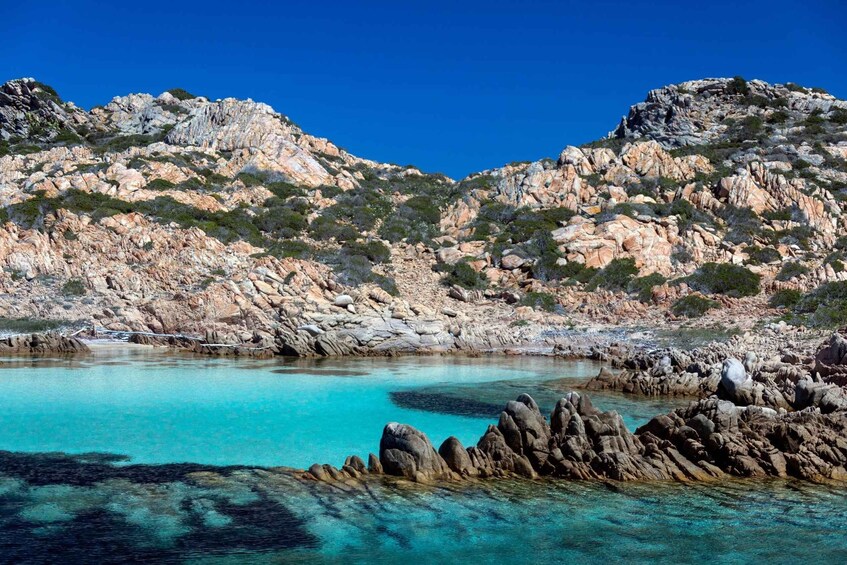 A rocky coastline with clear turquoise waters and sparse vegetation. 1