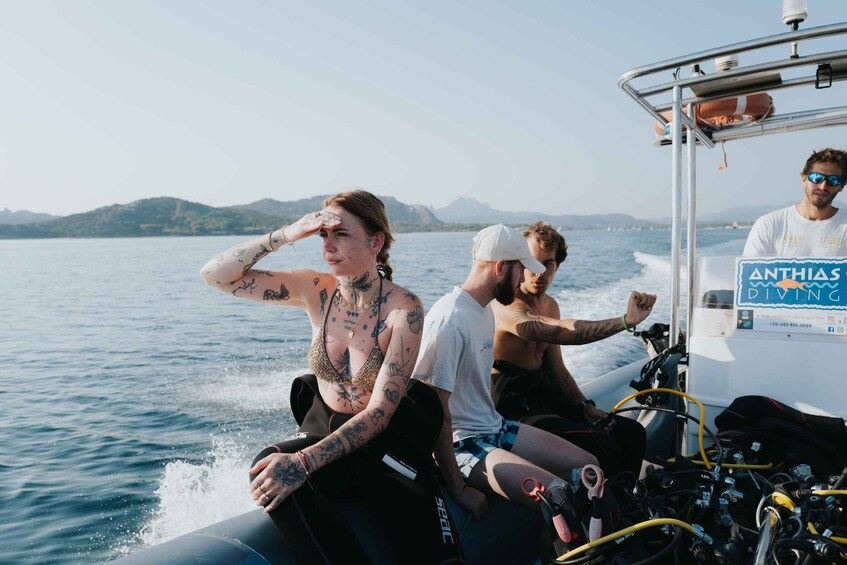 A boat with people on board, a sign reading 'ANTHIA'S DIVING,' and a body of water with mountains in the background. 3