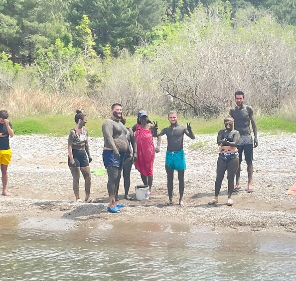 Un grupo de personas al borde de un río, algunas cubiertas de barro, con árboles y follaje al fondo. 4