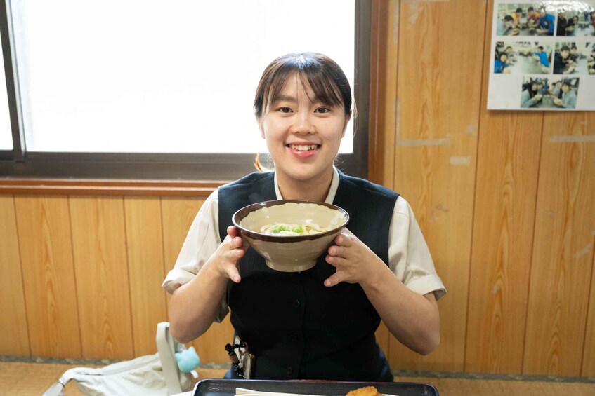 A person holding a bowl of ramen in a room with wooden walls and a window. 2