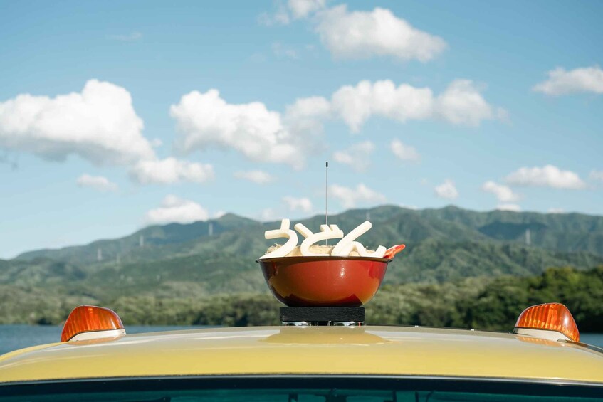 A car with a red bowl on its hood, a mountain range in the background, and a clear sky. 3