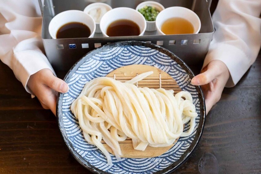 A person holding a plate with noodles and a tray of sauces. 4