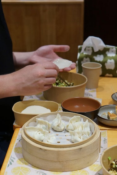 A person preparing dumplings on a table with various bowls and a steaming basket. 2