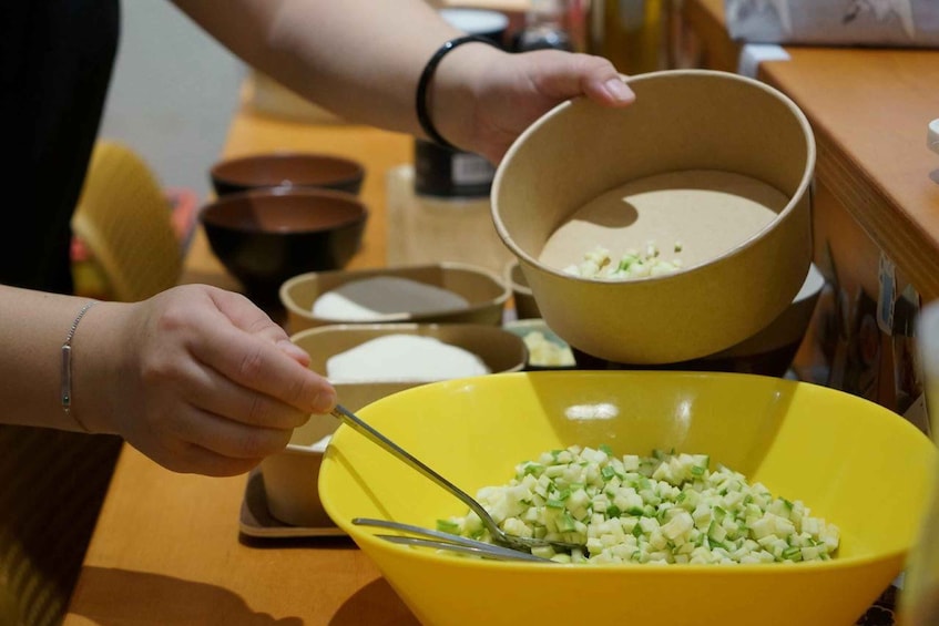 A person preparing food, with a yellow bowl containing chopped ingredients and a bowl of flour. 5
