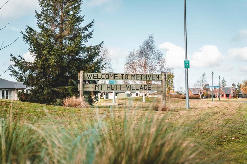 A welcome sign to Methven, MT Hutt Village, with a backdrop of trees and a clear sky. 1