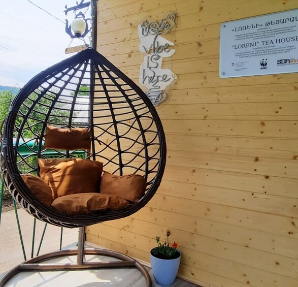 A hanging chair with cushions, a wooden wall with a sign, and a potted plant. 1
