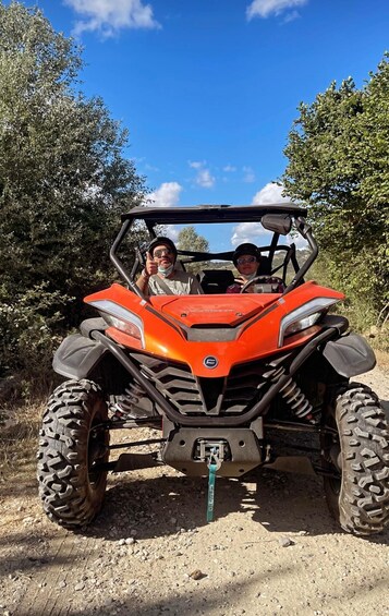 A red ATV with two people, one wearing a helmet, on a dirt path with trees and a clear sky in the background. 3