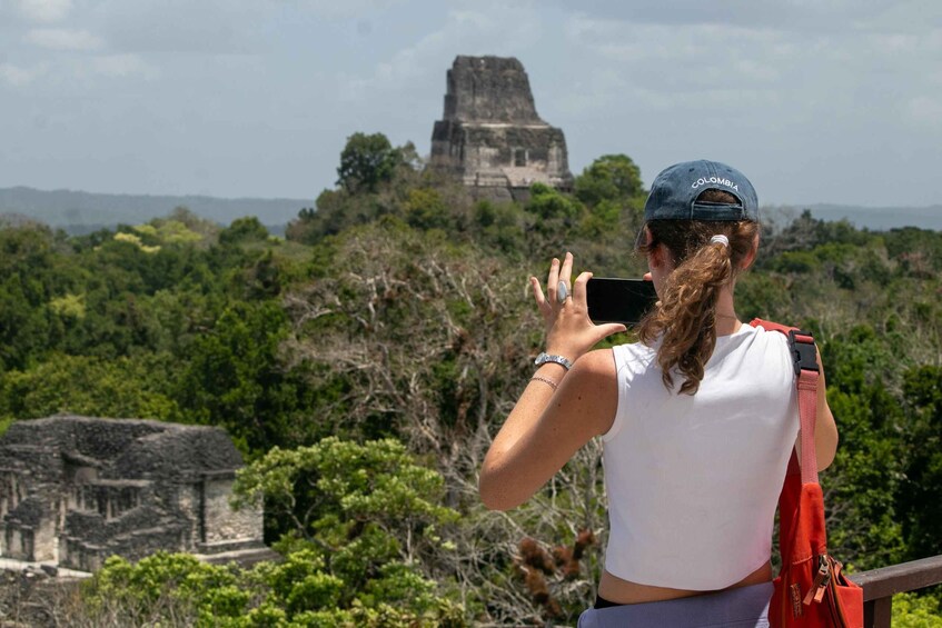 A person taking a photo of a Mayan pyramid with lush greenery in the background. 5