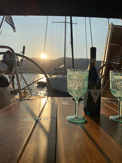A wooden table with a bottle of wine and two glasses, set against a backdrop of a sunset over a marina with sailboats. 4