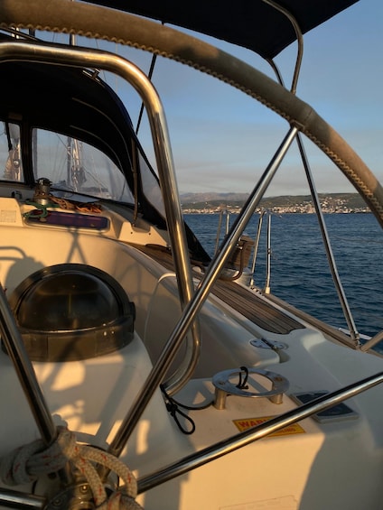 A sailboat's deck with metal railings, a steering wheel, and a view of a coastal town across the water. 3
