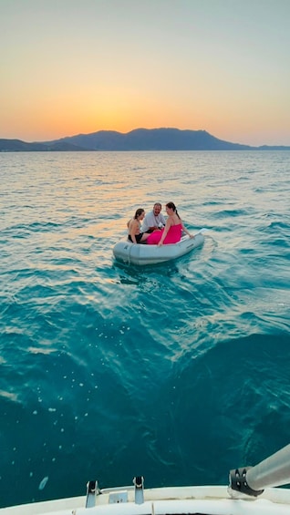 A group of people on a small inflatable raft in the middle of a body of water with a sunset in the background. 3