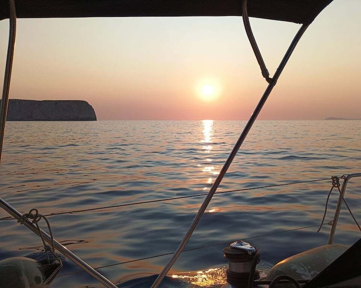 A sunset over calm waters with a boat's rigging and a distant cliff. 2