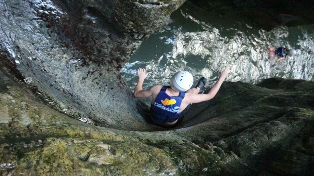 A person climbing a narrow, rocky water channel. 3