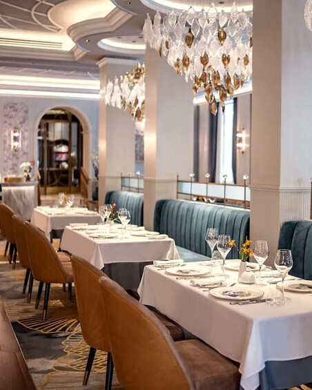 A restaurant interior with tables set for dining, upholstered booths, and a decorative chandelier. 1