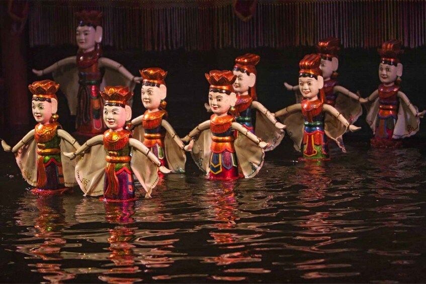 A group of performers in colorful costumes on a stage with a dark background. 3