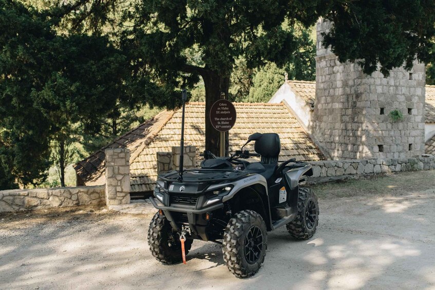 A black ATV parked on a gravel path with a stone wall and a sign in the background. 2