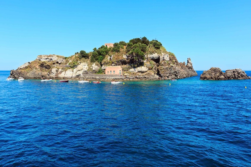 A rocky island with a small building surrounded by boats in the water. 5