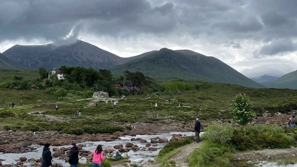 A mountainous landscape with a stream, a stone structure, and a few people. 3