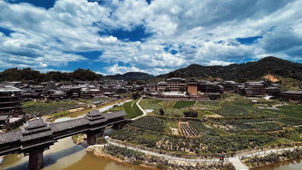 A traditional village with tiered buildings, a river, terraced fields, and mountains in the background. 4