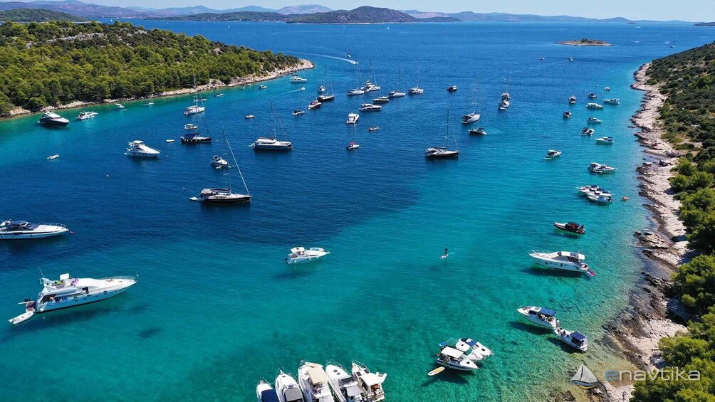 A coastal area with numerous boats anchored in clear turquoise waters, surrounded by lush greenery and rocky terrain. 1
