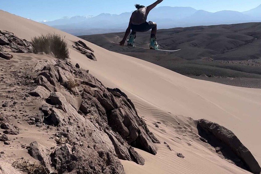 A person snowboarding down a sand dune with a mountainous landscape in the background. 5