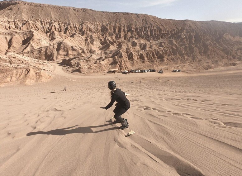 A person riding a dune buggy on sand dunes with a rocky mountain in the background. 1