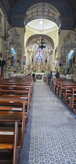An ornate church interior with pews, a tiled floor, and a central altar. 1