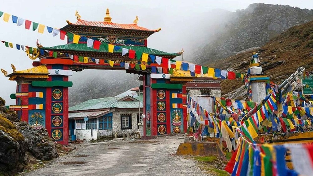 A traditional Tibetan gate with colorful prayer flags, a small building, and a mountainous backdrop. 3