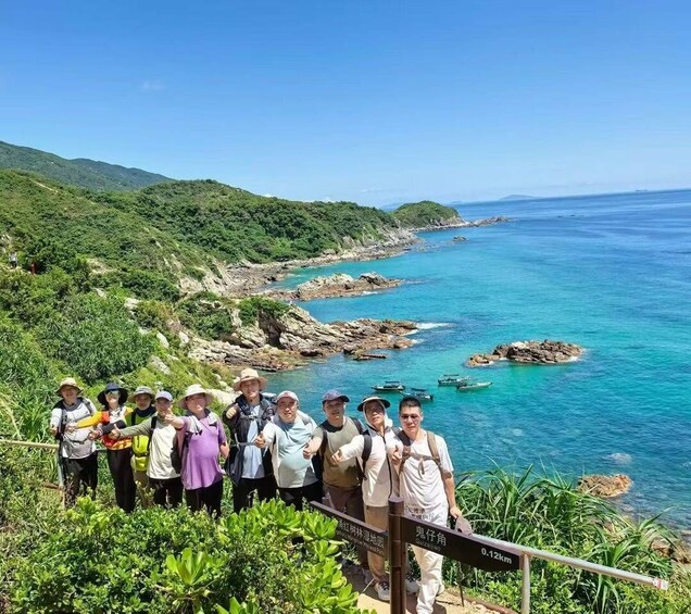 A group of people standing on a trail overlooking a coastal area with clear blue water and green hills. 1