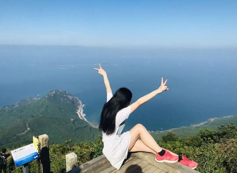 A person sitting on a wooden platform overlooking a coastal landscape with greenery and a clear view of the sea. 1
