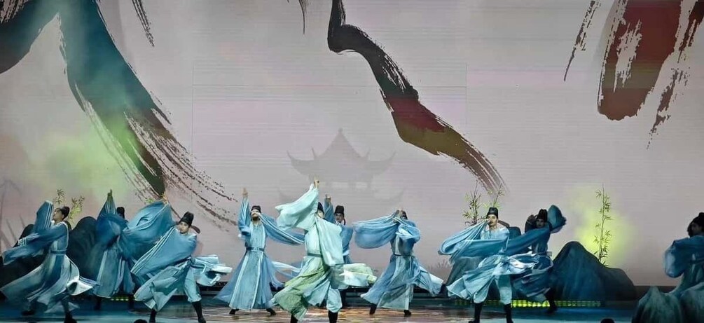 A group of performers in traditional blue costumes on a stage with a backdrop of Chinese-style architecture and brushstroke art. 2
