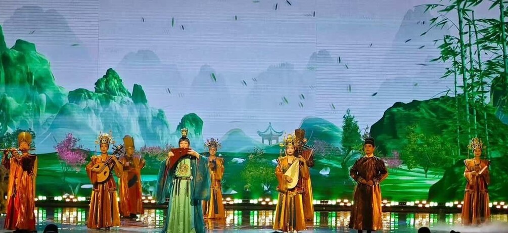 A stage with performers in traditional costumes, a backdrop of mountains and water, and a traditional pavilion. 5