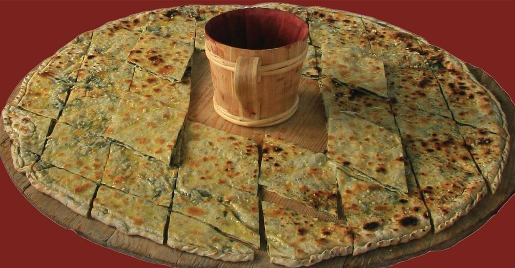 A large, round flatbread with a wooden bowl in the center, cut into triangular pieces. 2