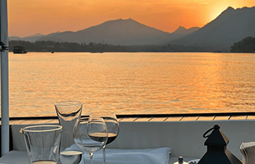 A table with wine glasses and a candle, overlooking a sunset over a lake with mountains in the background. 4