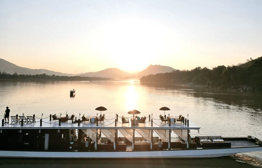 A riverboat with tables and chairs, a person standing, and a boat in the distance. 3