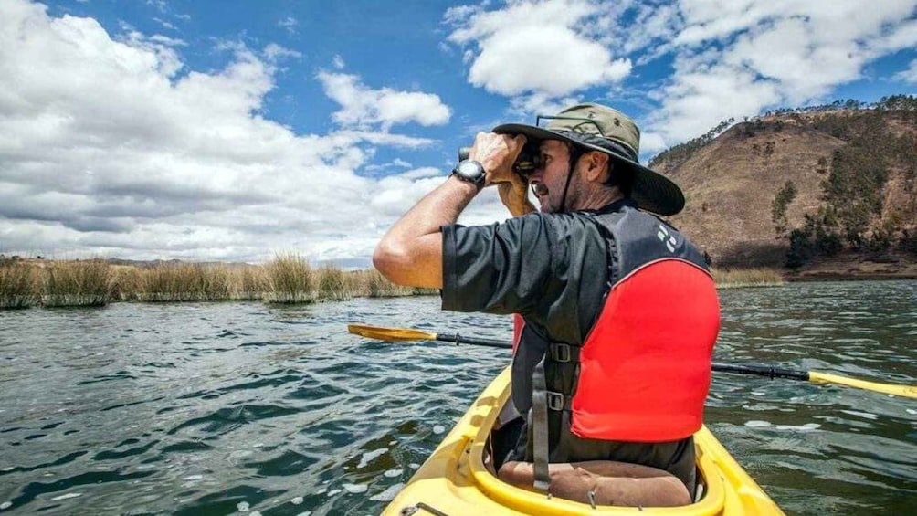 A person kayaking on a river with a red life jacket, surrounded by water and a hilly landscape. 2