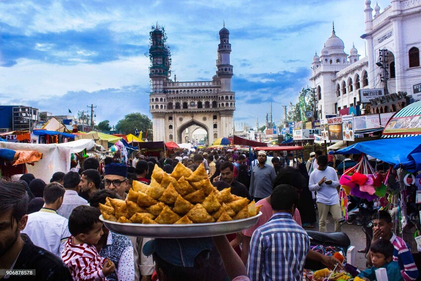 A busy market with people and a large plate of samosas. 1