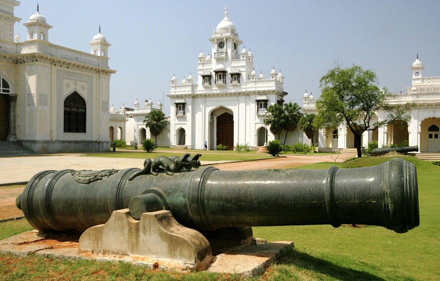 A large cannon in front of a white building with domes and arches. 2