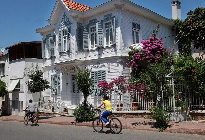 A white building with blue shutters, a person riding a bicycle, and pink bougainvillea flowers. 4