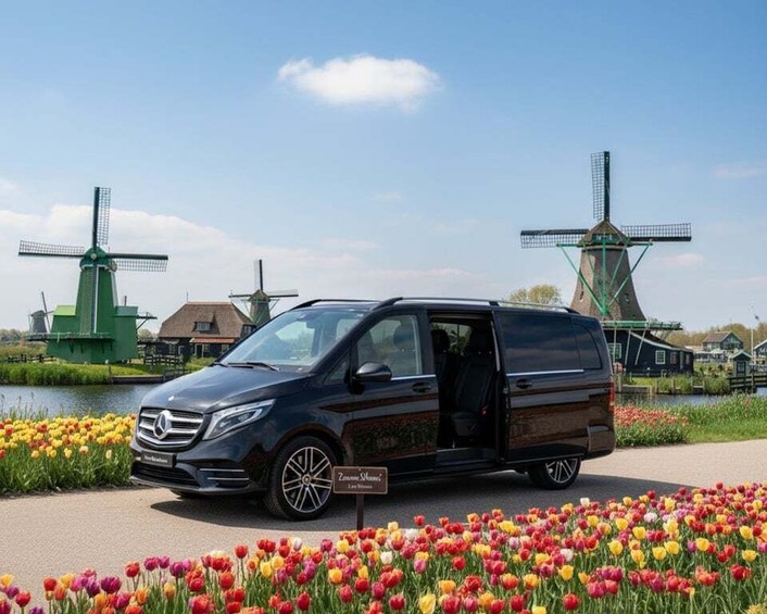 A black van parked on a road with a tulip field and windmills in the background. 1
