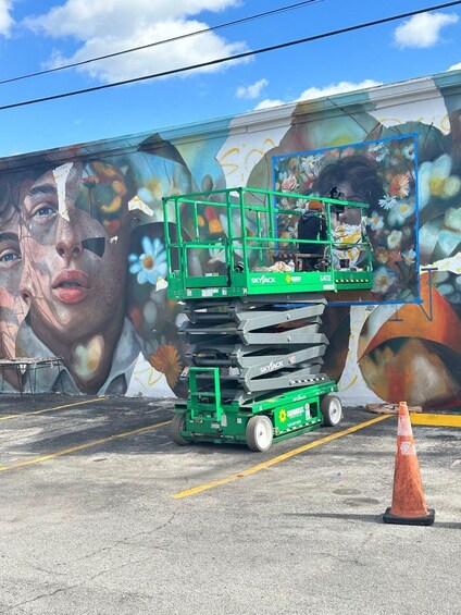 Una piattaforma elevatrice Skyjack verde di fronte a un murale con motivi floreali e astratti. 3