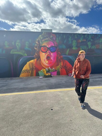 Una persona in piedi di fronte a un murale colorato con una figura grande e un veicolo. 4