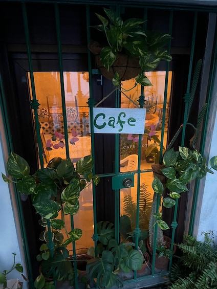 A cafe entrance with a sign, potted plants, and a metal gate. 2